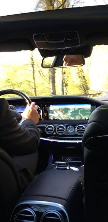 Homme en costume conduisant une voiture avec un ciel dégagé visible à travers le toit.